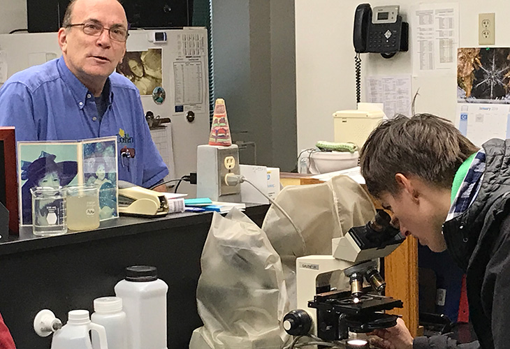 MAEE Student Sarah Gothe views an amoeba through a microscope while wastewater staff describe mercury regulations.