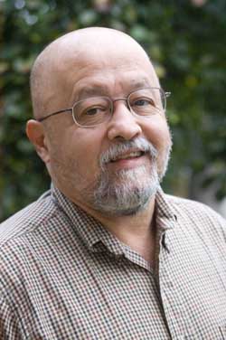 balding male with wire-rimmed glasses, a brown checkered shirt, smiling at the camera.