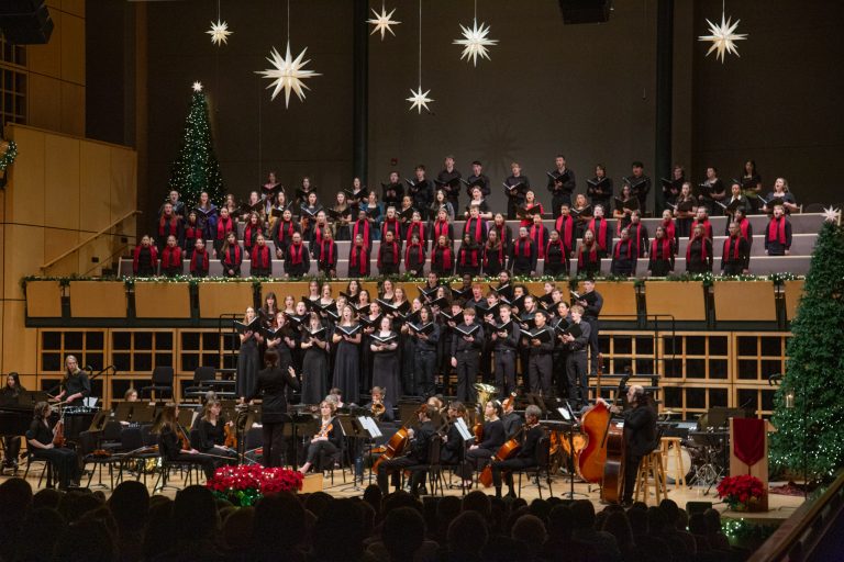 Choirs and orchestra fill the stage beneath stars and a Christmas tree