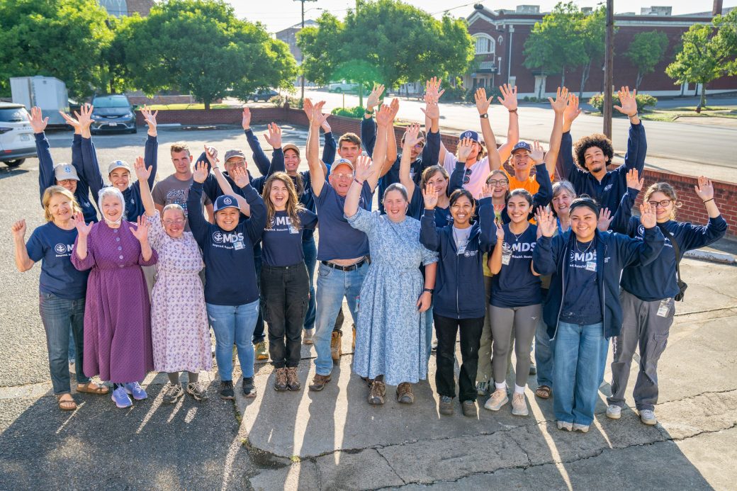 Group of students with matching t-shirts lifting their arms up and smiling