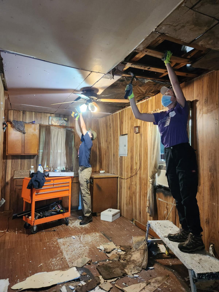 Two students work on disassembling a ceiling, surrounded by fallen ceiling and plaster.