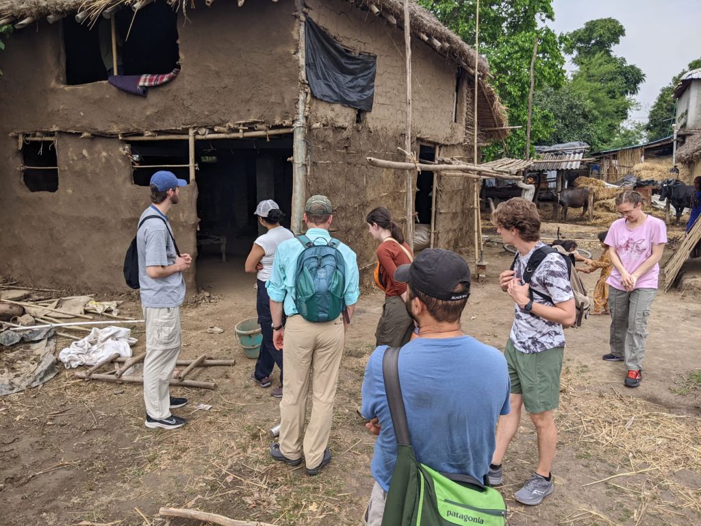 Students inspect a two-story building that appears to be made from logs and hardened mud.