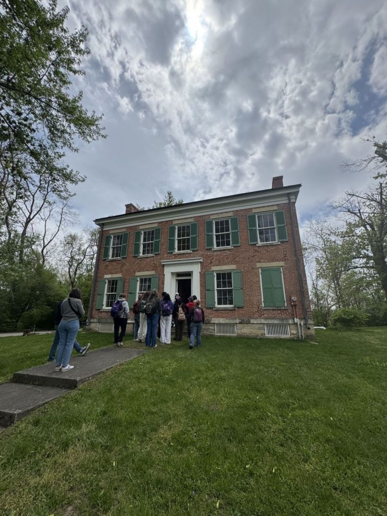 A group of students stands in front of a two-story brick house.