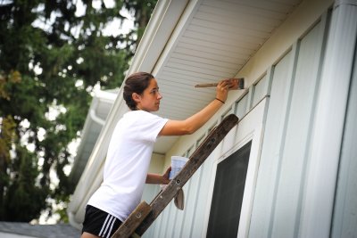 Girl standing on ladder painting a building
