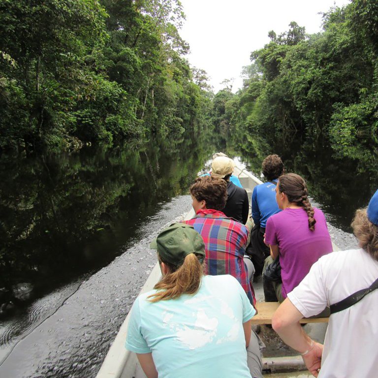 students on a boat going down a jungle river