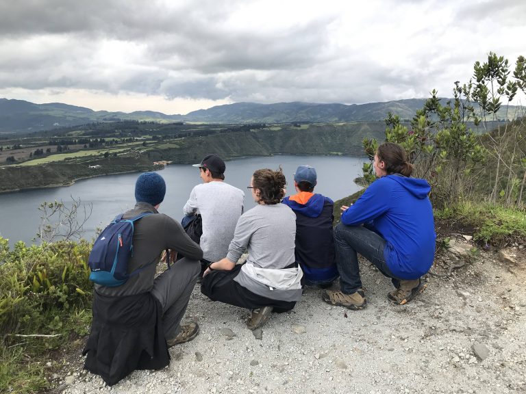 students crouched in front of scenic view, facing away from camera