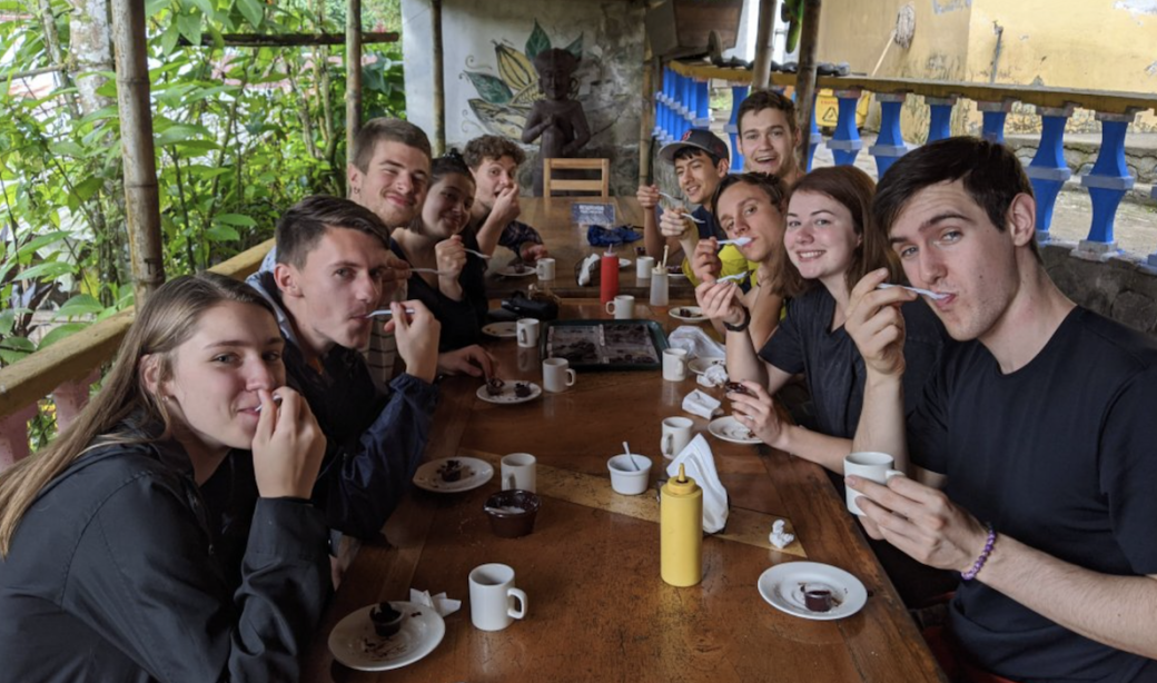 study abroad group of students eating at a long table looking at camera