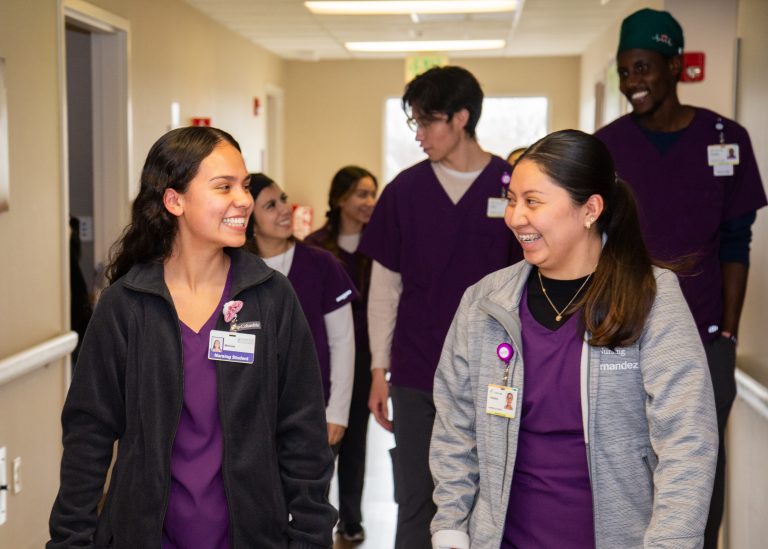 Students in scrubs smiling at eachother