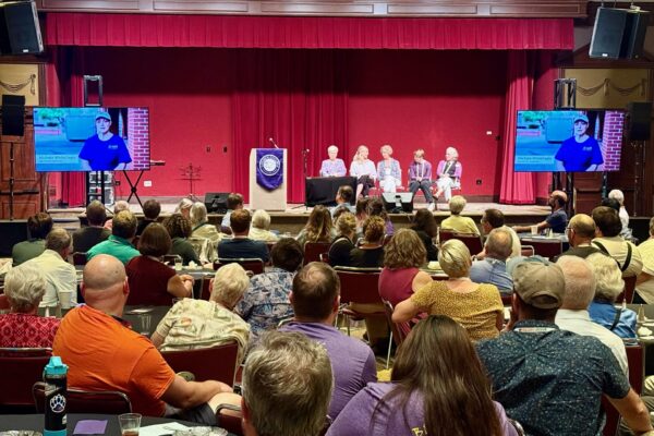 A panel speaks on stage in front of a large group of people.