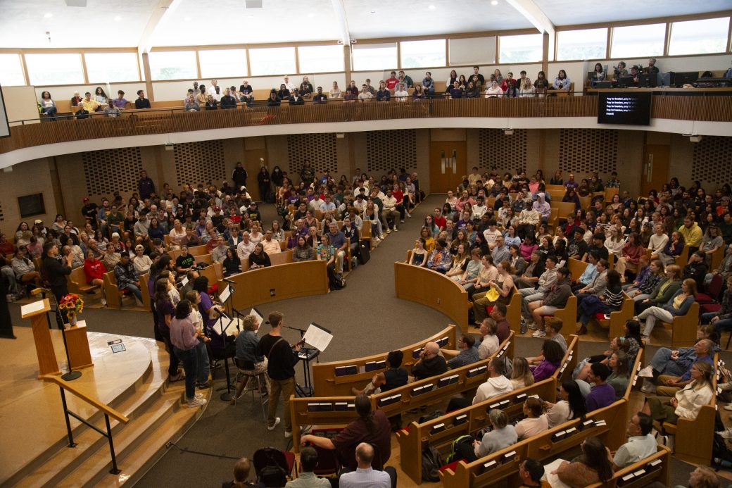 A group of about ten people sings to a packed hall.
