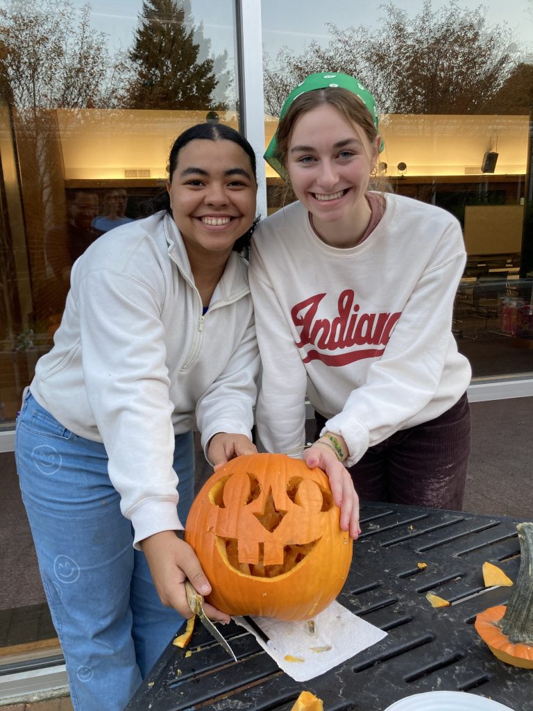 Two students smile holding a jack'o'lantern