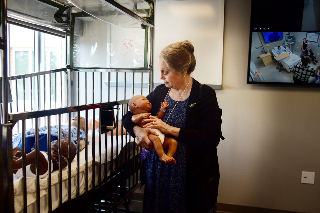 woman sits holding an infant manikin