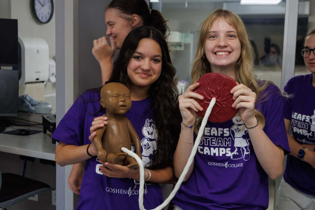 Two campers holding baby mannequin and smiling