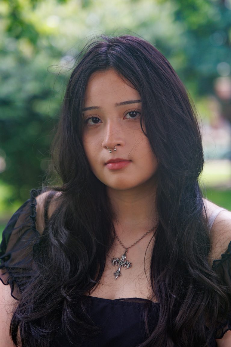 Professional headshot of Sara Nunez wearing an off the shoulder black top and a large silver cross necklace.