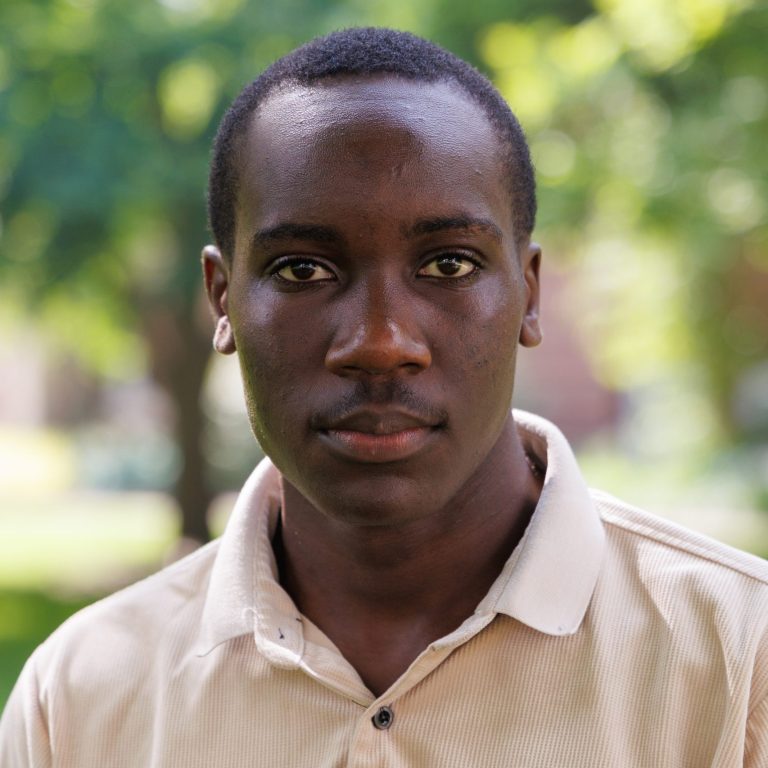Professional headshot of Timothy Okiror wearing a beige polo shirt.