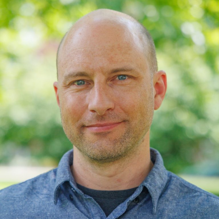 Professional headshot of Andrew Clouse outside in August 2026. He is wearing a blue linen button up.