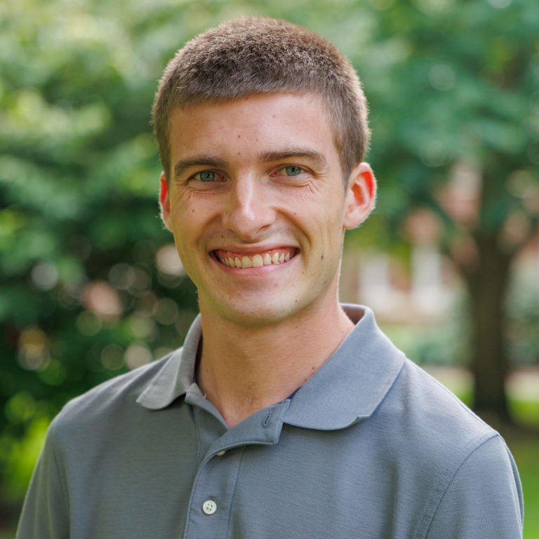 Updated headshot of Justin DeWeese. He is wearing a grey polo and is smiling at the camera head on.