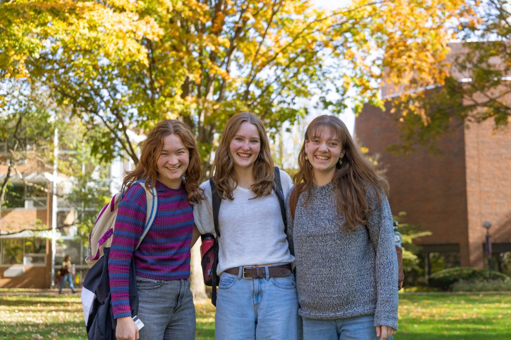 Three smiling students with fall backdrop