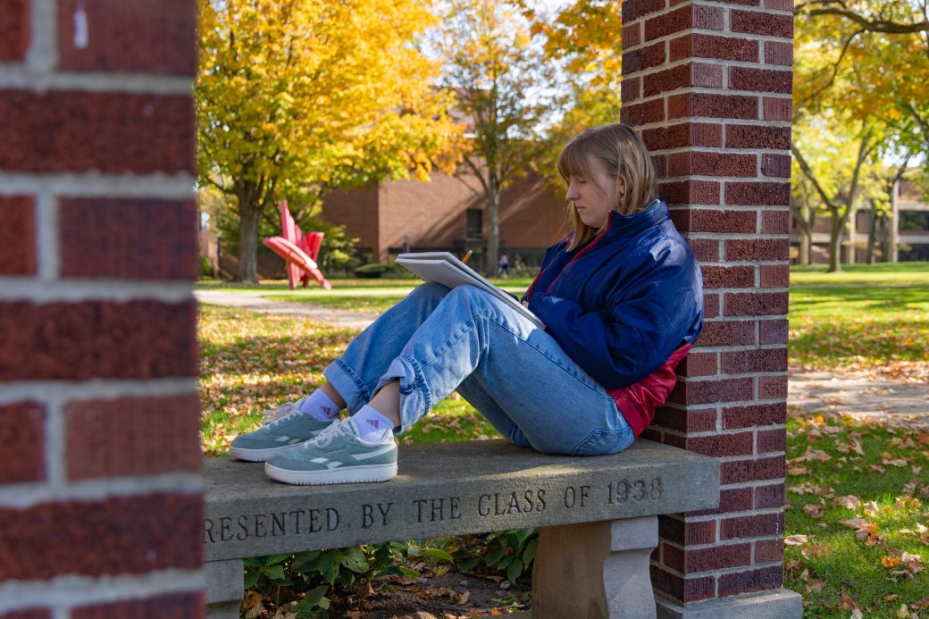 Student drawing on bench by shield