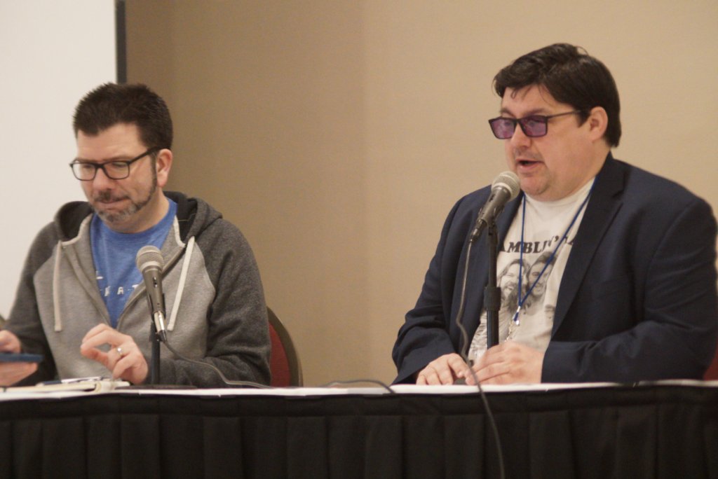 Two men sitting at a table and speaking into microphones