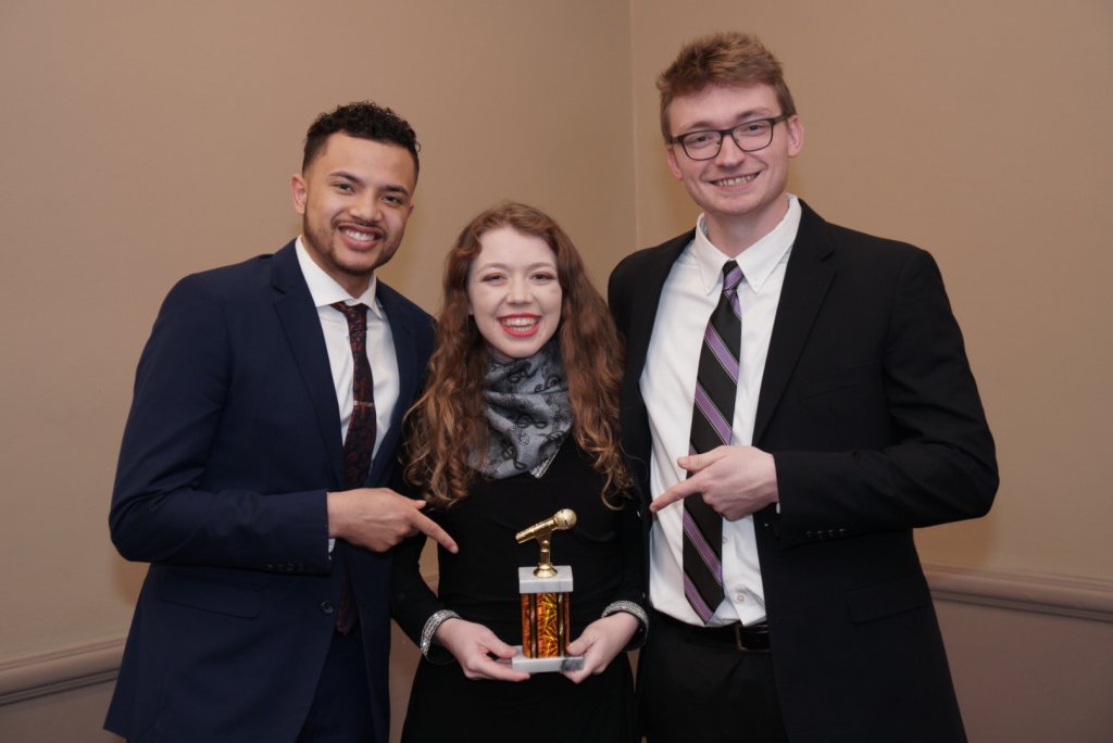 Two men posing for a photo with a woman who is holding an award