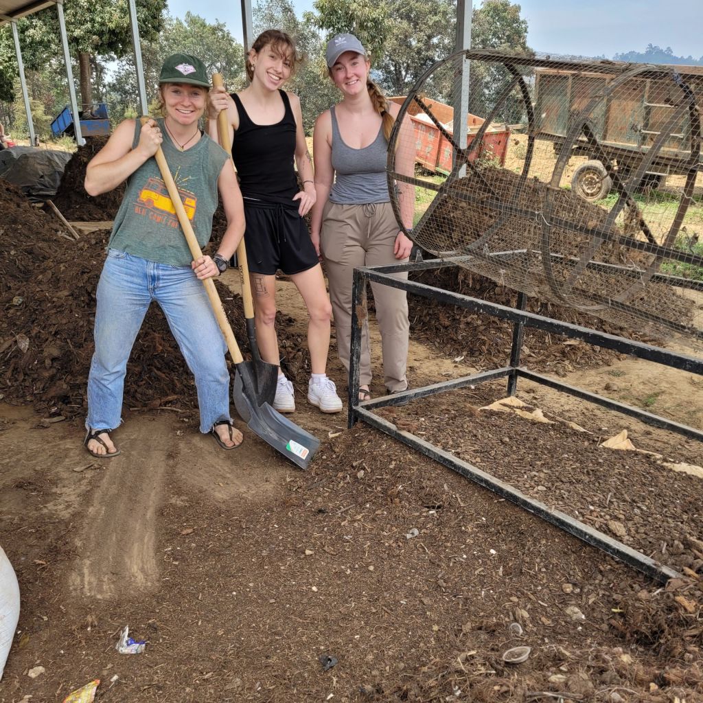 Three young people pose in work clothes with tools and a sifter.