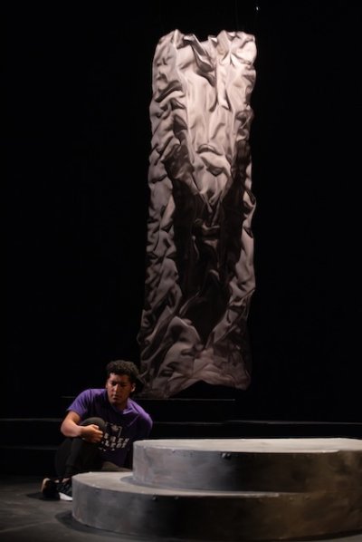 a large gray cloth has unraveled or fallen, from the ceiling to the floor in the background of the stage