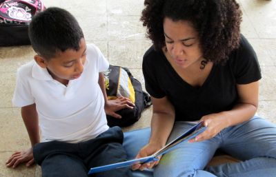 Cora helps a student read a book.