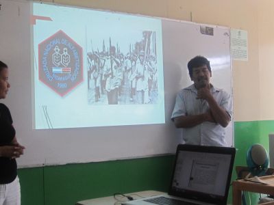 Humberto showing the logo of the campaign and a photo of young brigadistas marching (with oversized pencils) in the "war against illiteracy."