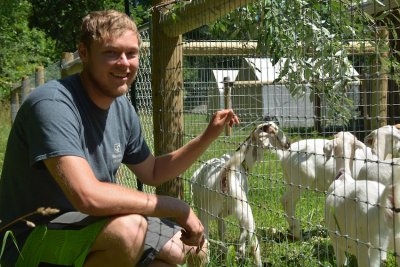 Man kneeling next to goats in a pen