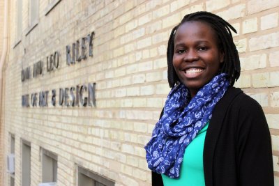 Woman wearing a blue scarf smiling, standing next to a building