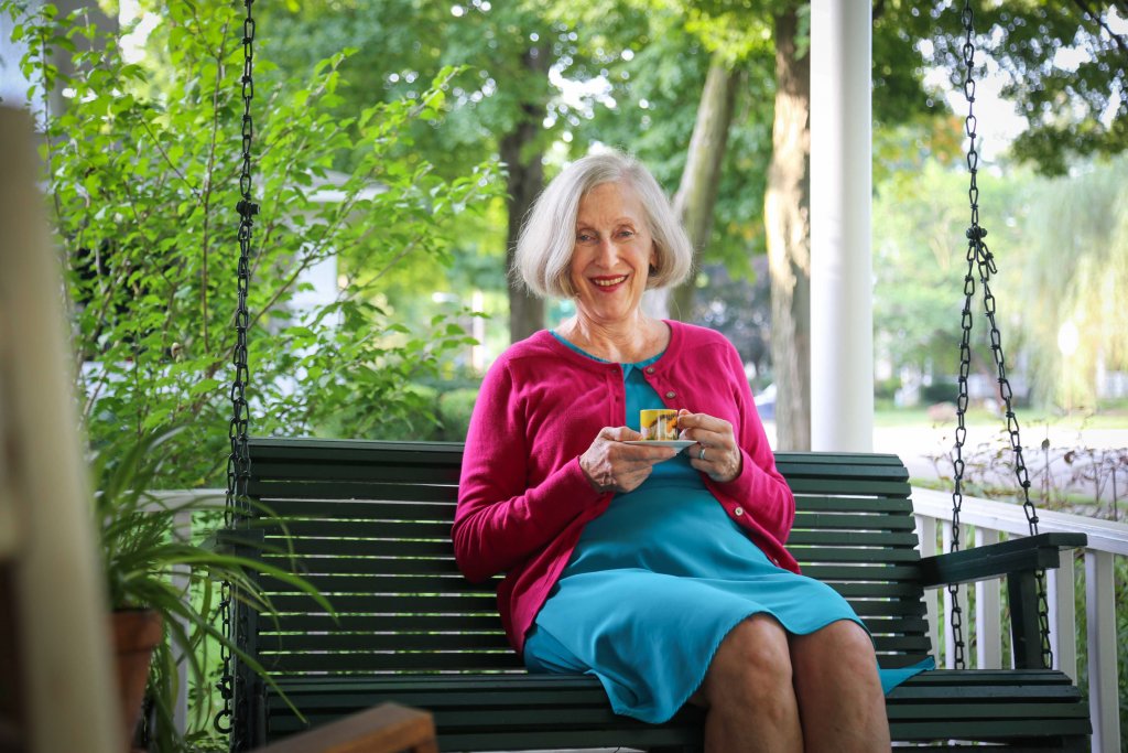 Woman sitting in a porch bench smiling while holding a cup and saucer
