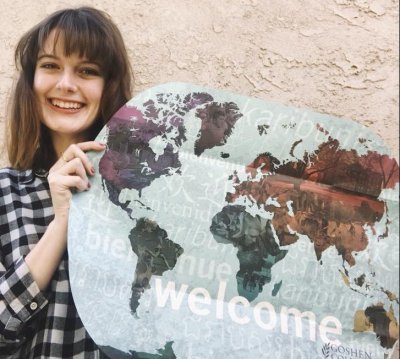 Woman in a black plaid shirt holding a map of the world with the Goshen College logo