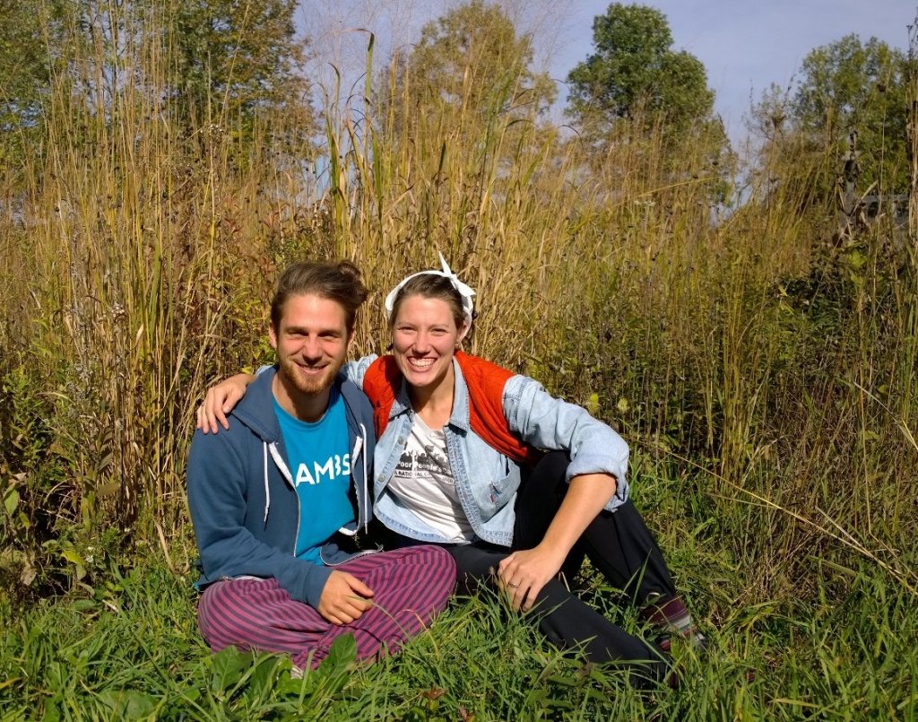 Two students posing together on the ground surrounded by prairie grass