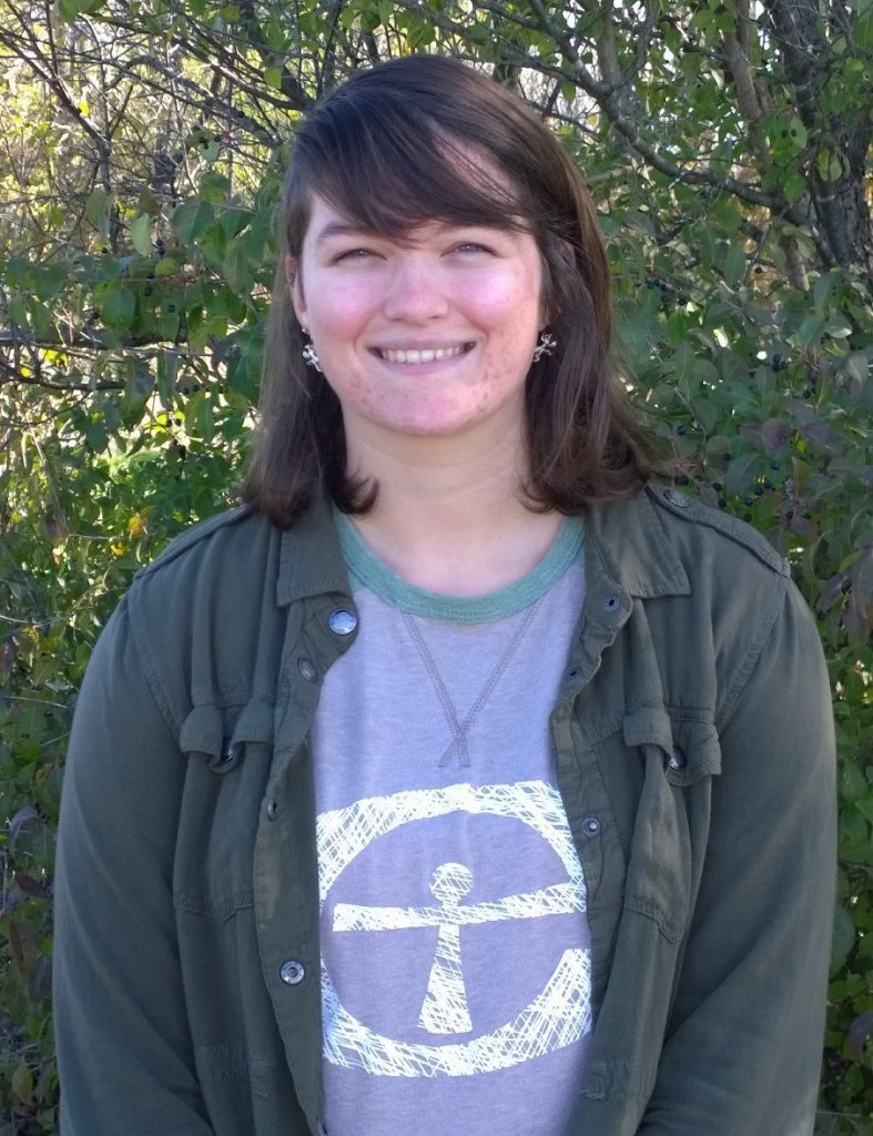 Woman in a green jacket, gray and green Merry Lea shirt smiling in front of a tree