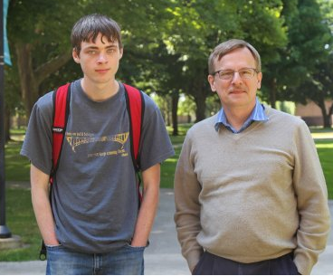 Student in a gray t-shirt standing next to a professor in a tan sweater