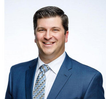 Headshot of a man in a dark blue jacket smiling