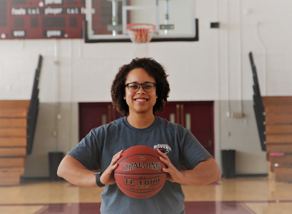 Woman in a dark gray t-shirt holding a basketball in a basketball court