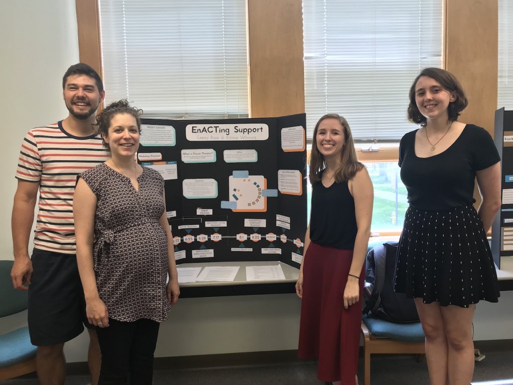 Three students and a professor standing next to their presentation