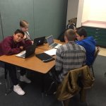 Middle school students sitting at a desk working on laptops