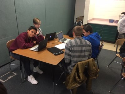 Middle school students sitting at a desk working on laptops