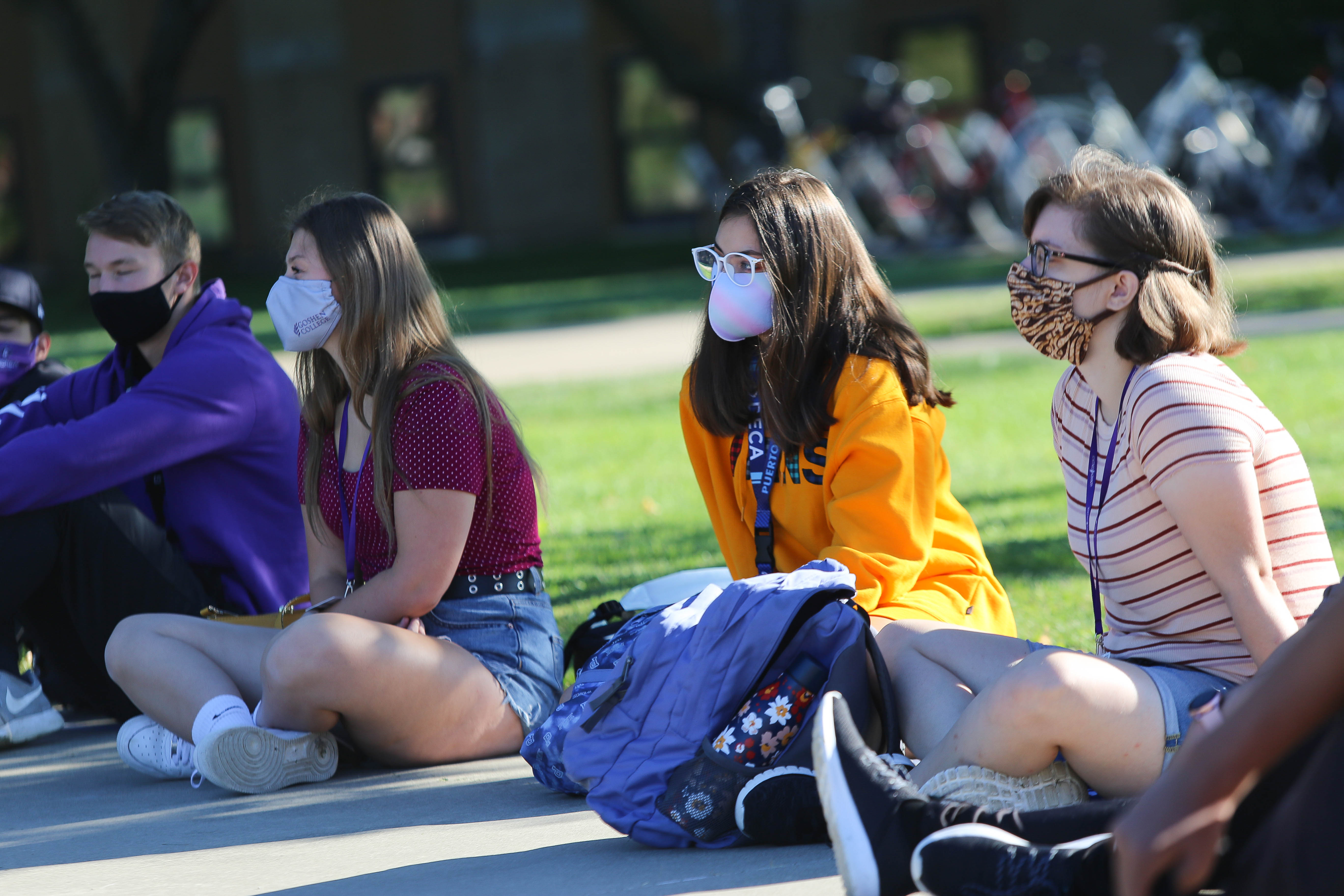 Students wearing masks sitting on the sidewalk