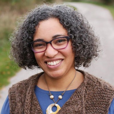 Woman wearing brown wool vest, glasses and necklace smiling