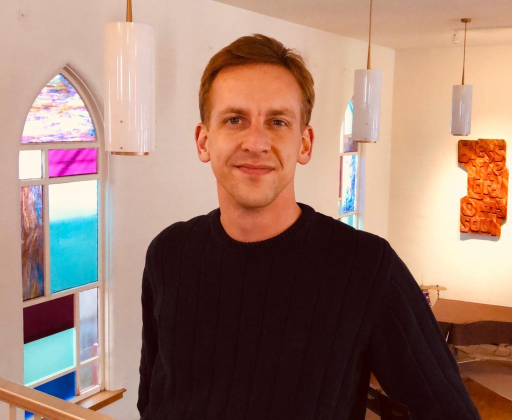 Man in a black sweater smiling in the upper level of a church.
