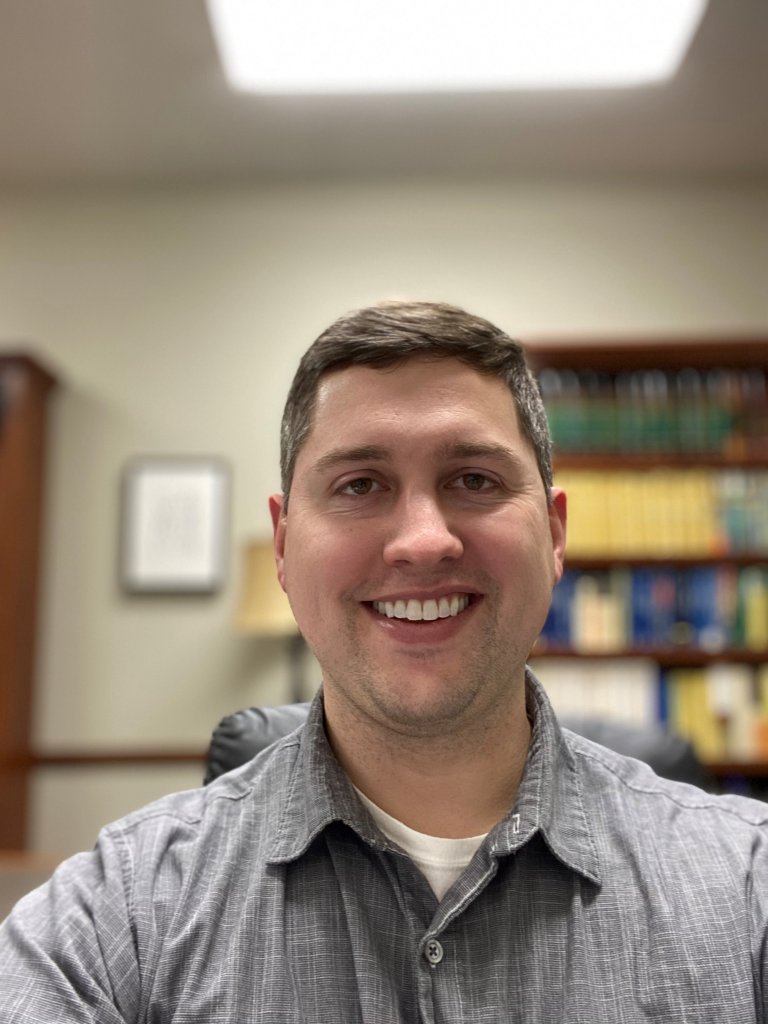 Man wearing a gray button up shirt smiling in an office