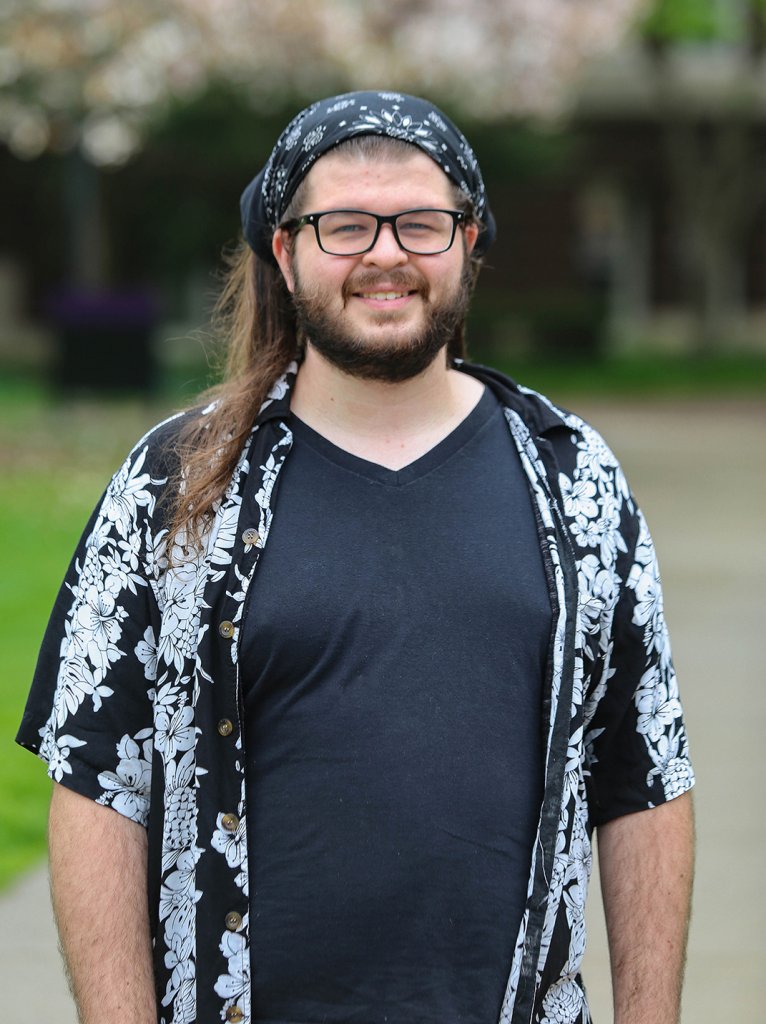 Man in a black shirt with white plants, black bandana and glasses smiling