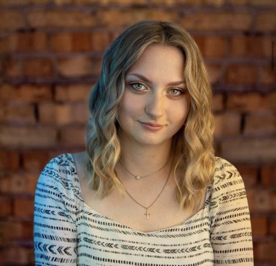 Woman in a white shirt with black arrow pattern smiling in front of a brick wall