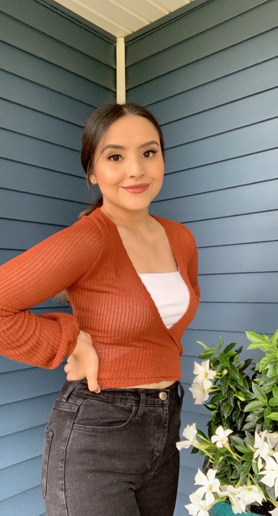 Woman in orange shirt, smiling by a flower pot