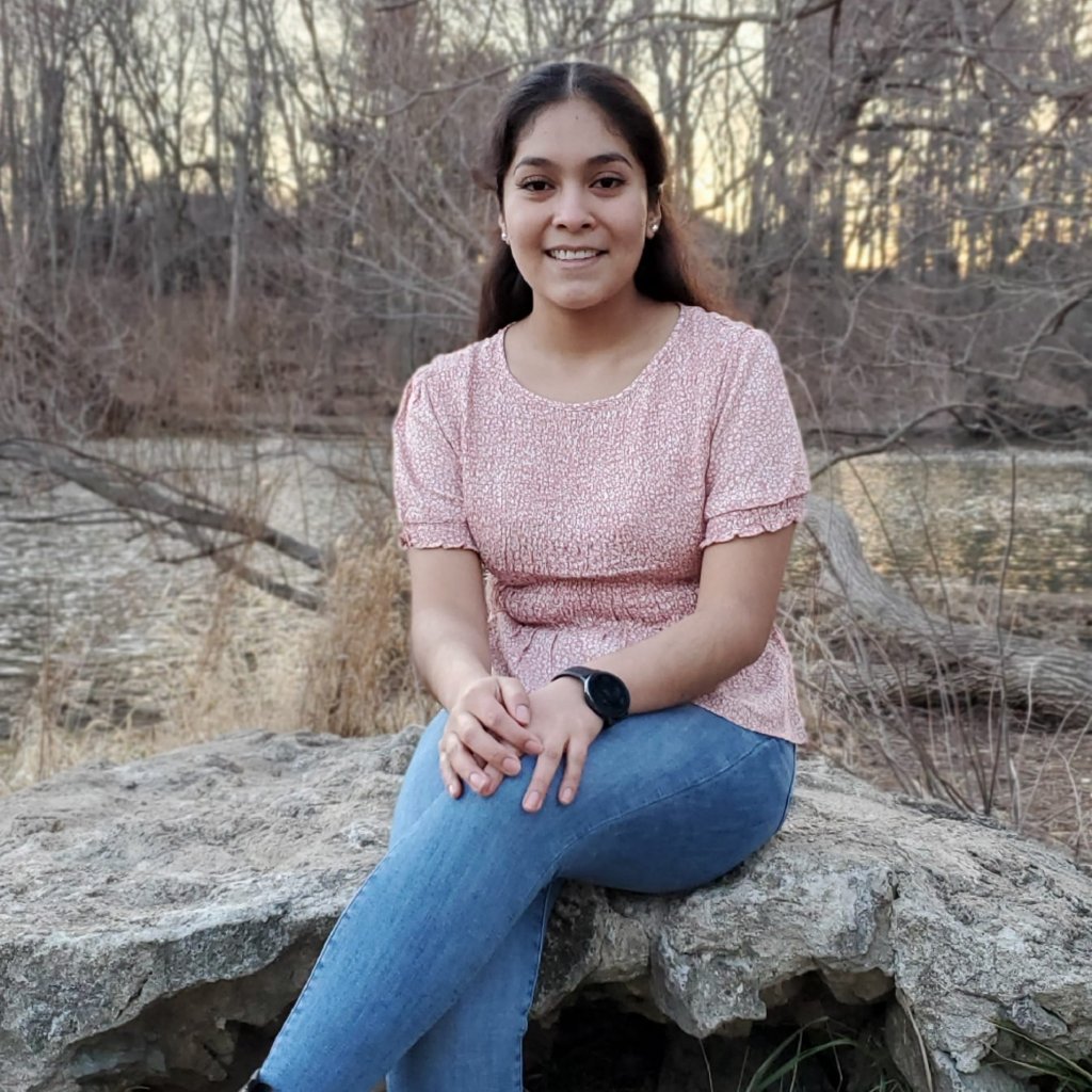 Woman in a pink shirt smiling, sitting on a rock