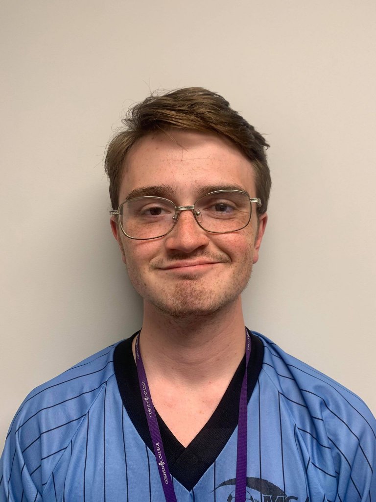 Man in a blue shirt with black stripes, purple lanyard and glasses smiling